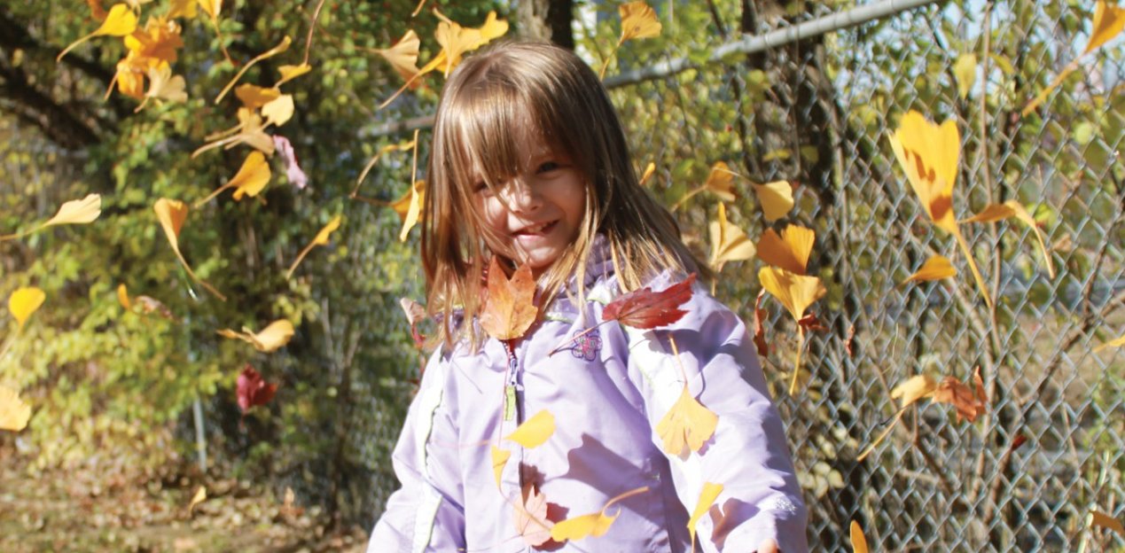 girl in jacket outside with leaves falling around her